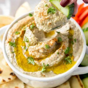 A cucumber digging into a bowl of homemade baba ghanouj