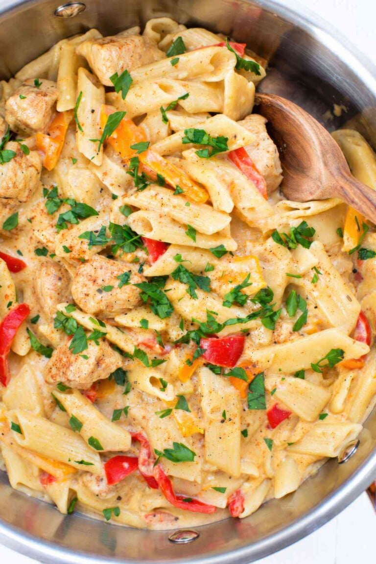 Close-up of penne, chicken chunks, and red and orange bell peppers coated in creamy Cajun sauce and topped with chopped parsley.