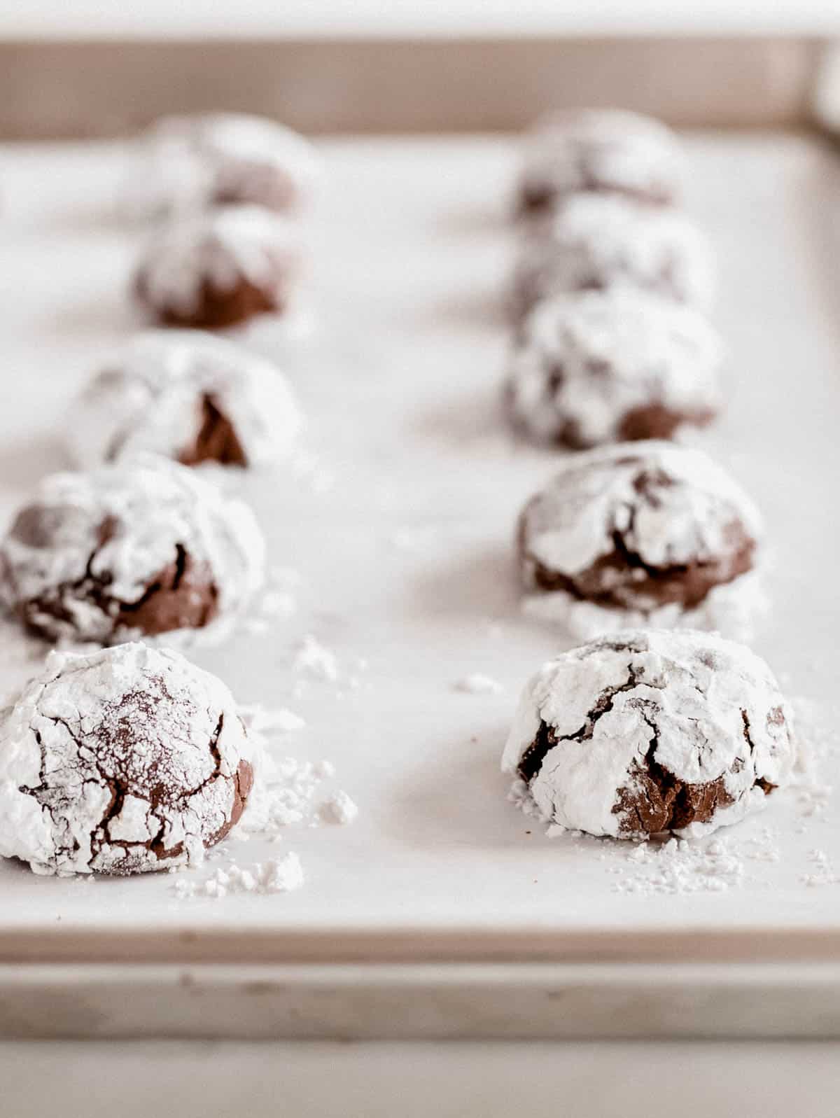 ten chocolate crinkle cookies on a piece of parchment paper on a baking sheet