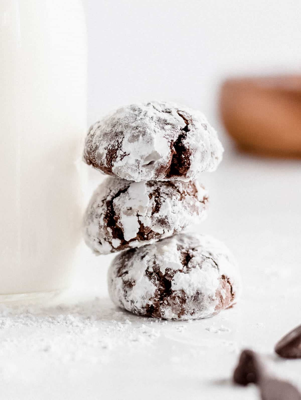 a stack of three chocolate crinkle cookies sitting next to a glass of milk