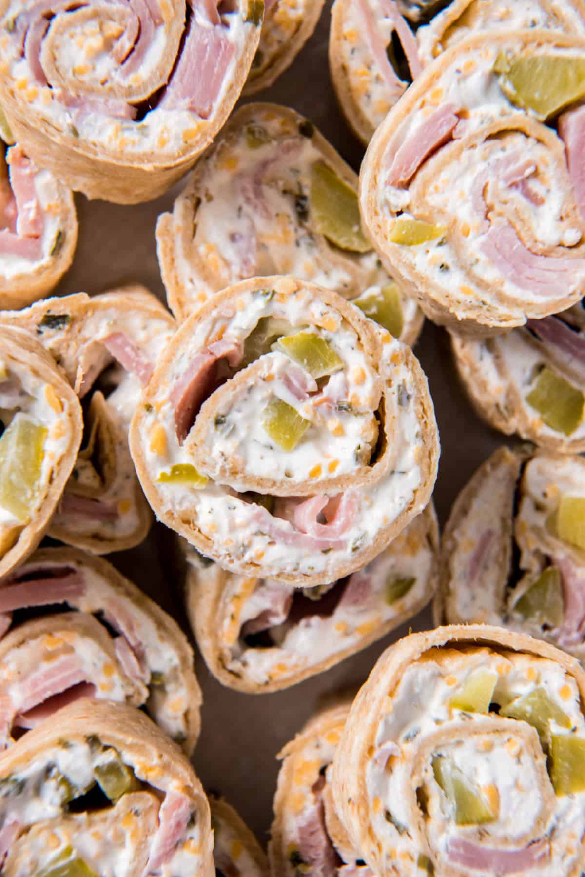 Close up photo of of ham and cheese pinwheels sitting stacked on a plate for serving.