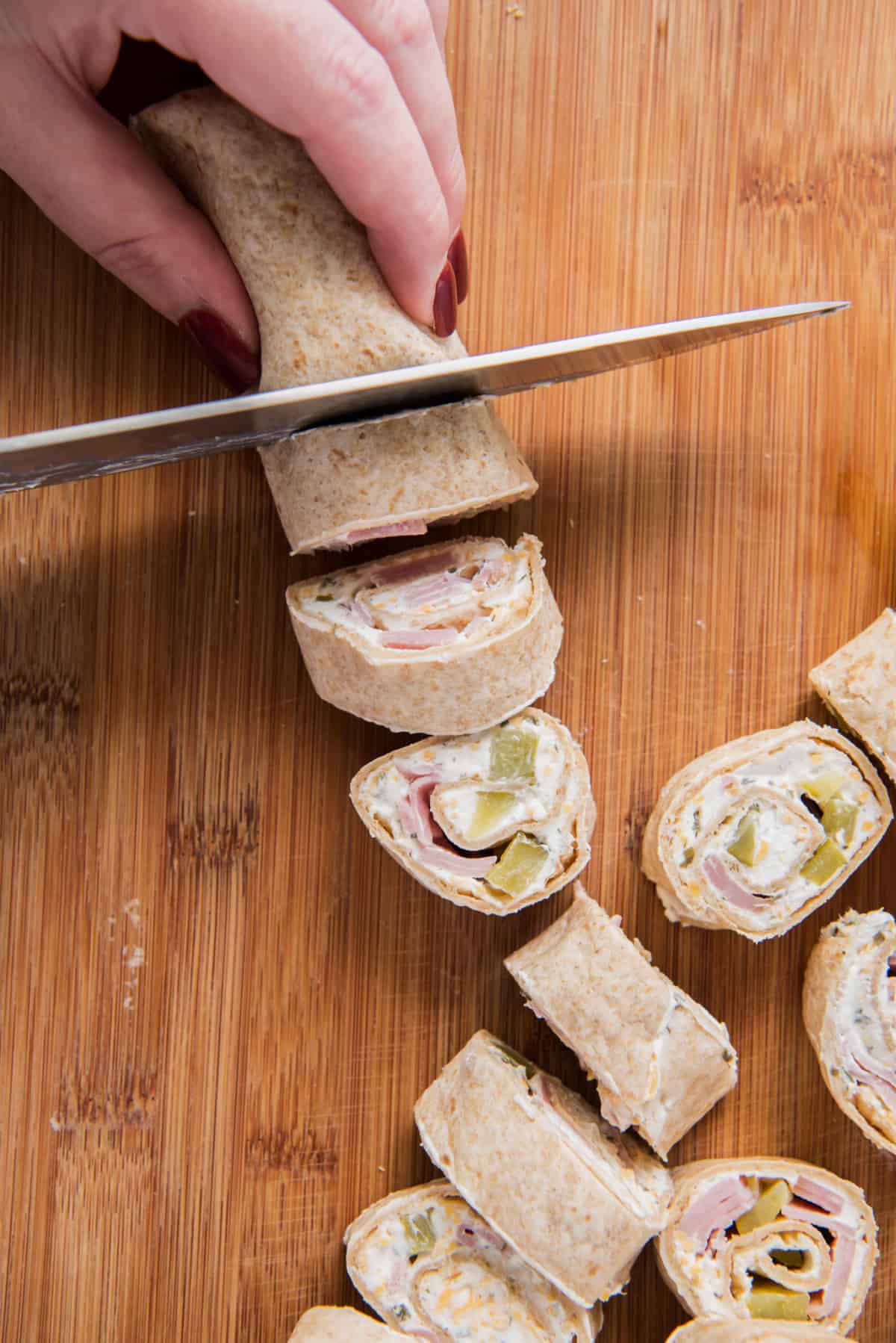 A knife slicing the rolled tortilla into mini pinwheels.