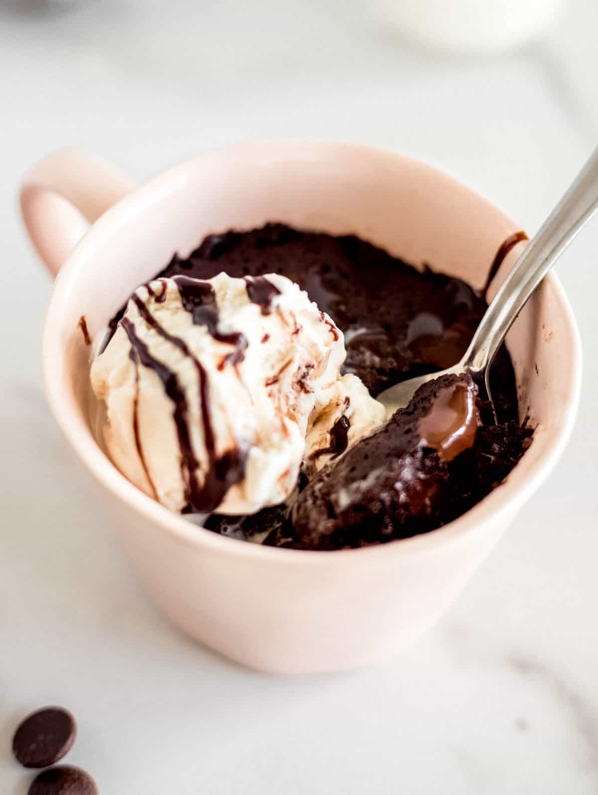 a spoon sitting in a mug with a chocolate brownie and scoop of vanilla ice cream