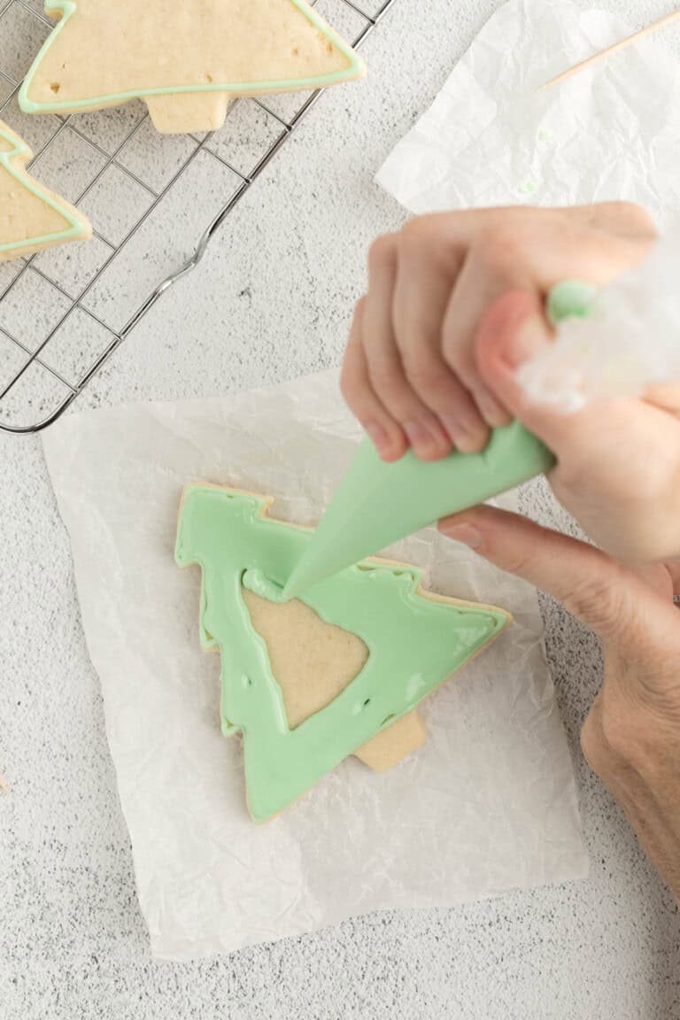holding a piping bag in one hand to fill the cookies with royal icing