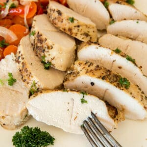 Sliced baked turkey tenderloin on a plate with the cooked carrots, peppers and onions. A fork sticks into a piece of turkey tenderloin before eating.