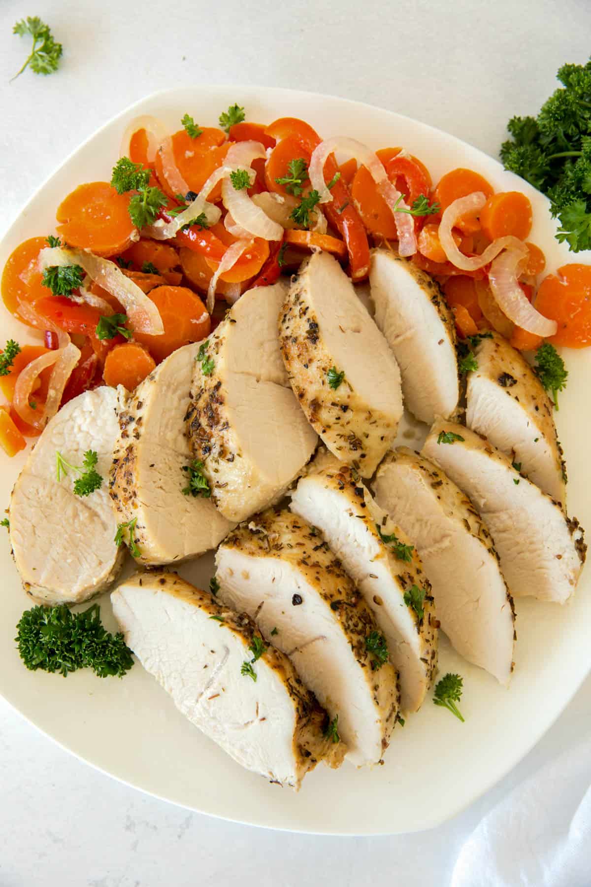 Baked easy turkey tenderloin sliced on a plate and served with carrots, peppers and onions.