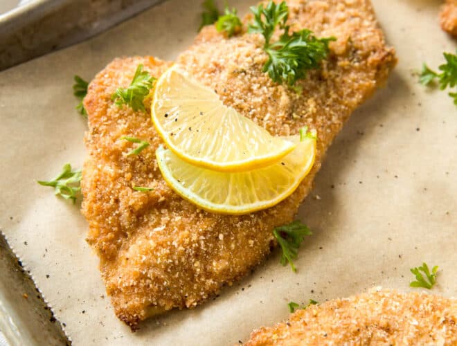 A few baked chicken cutlets on a baking sheet after baking in the oven.