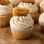 Close-up square crop of a cupcake with swirled frosting and a mini churro on top.