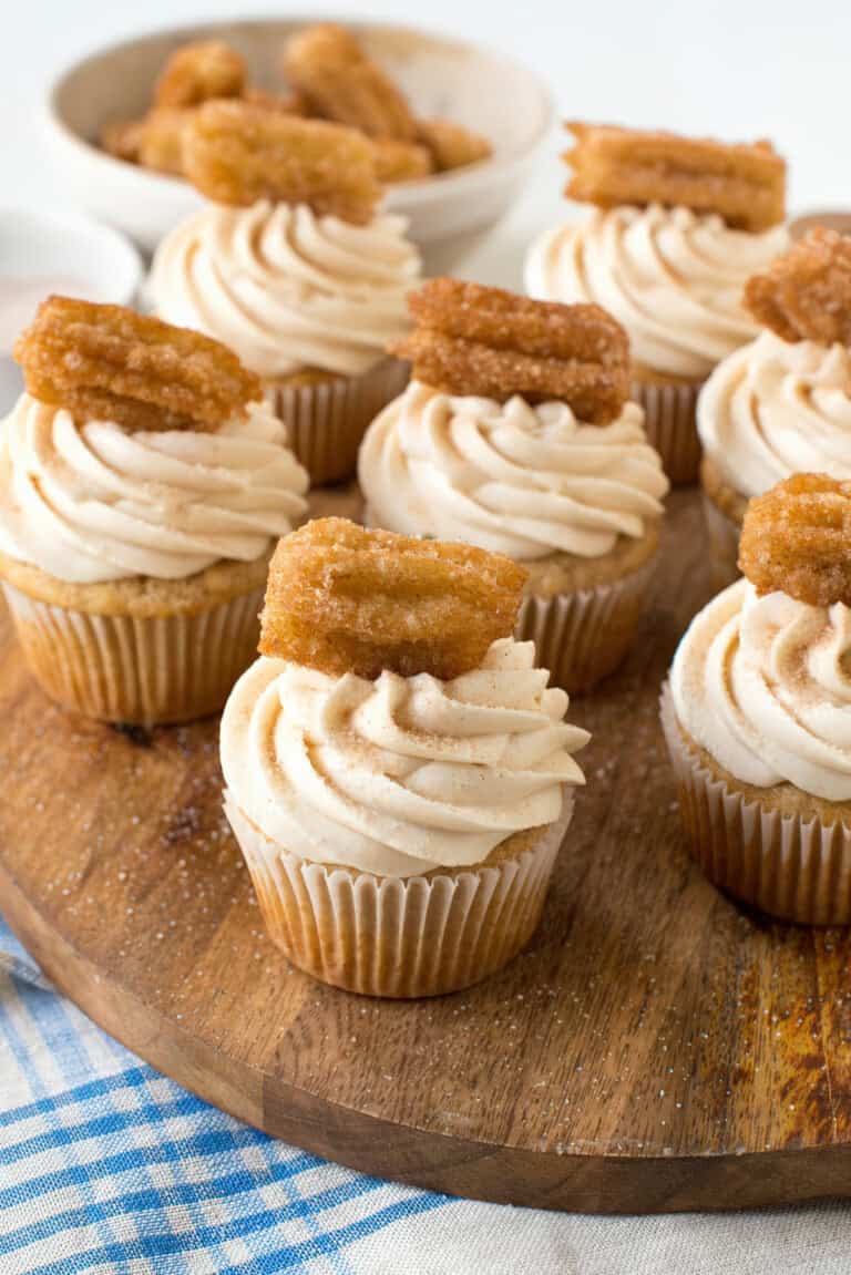 Churro cupcakes arranged on a wooden surface with a checkered napkin in the background.