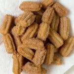 A close-up overhead view of a pile of sugar-coated mini churros on a paper towel/