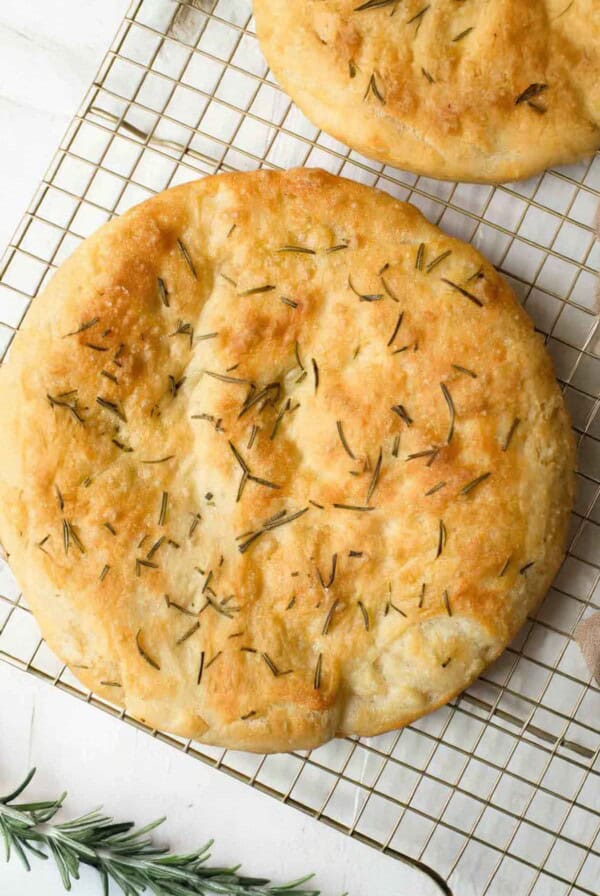 loaf of rosemary focaccia on a cooling rack with rosemary springs