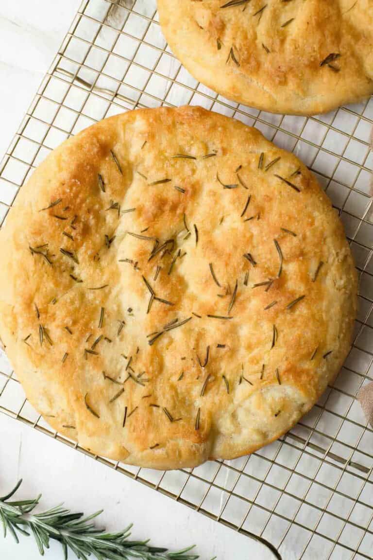 loaf of rosemary focaccia on a cooling rack with rosemary springs