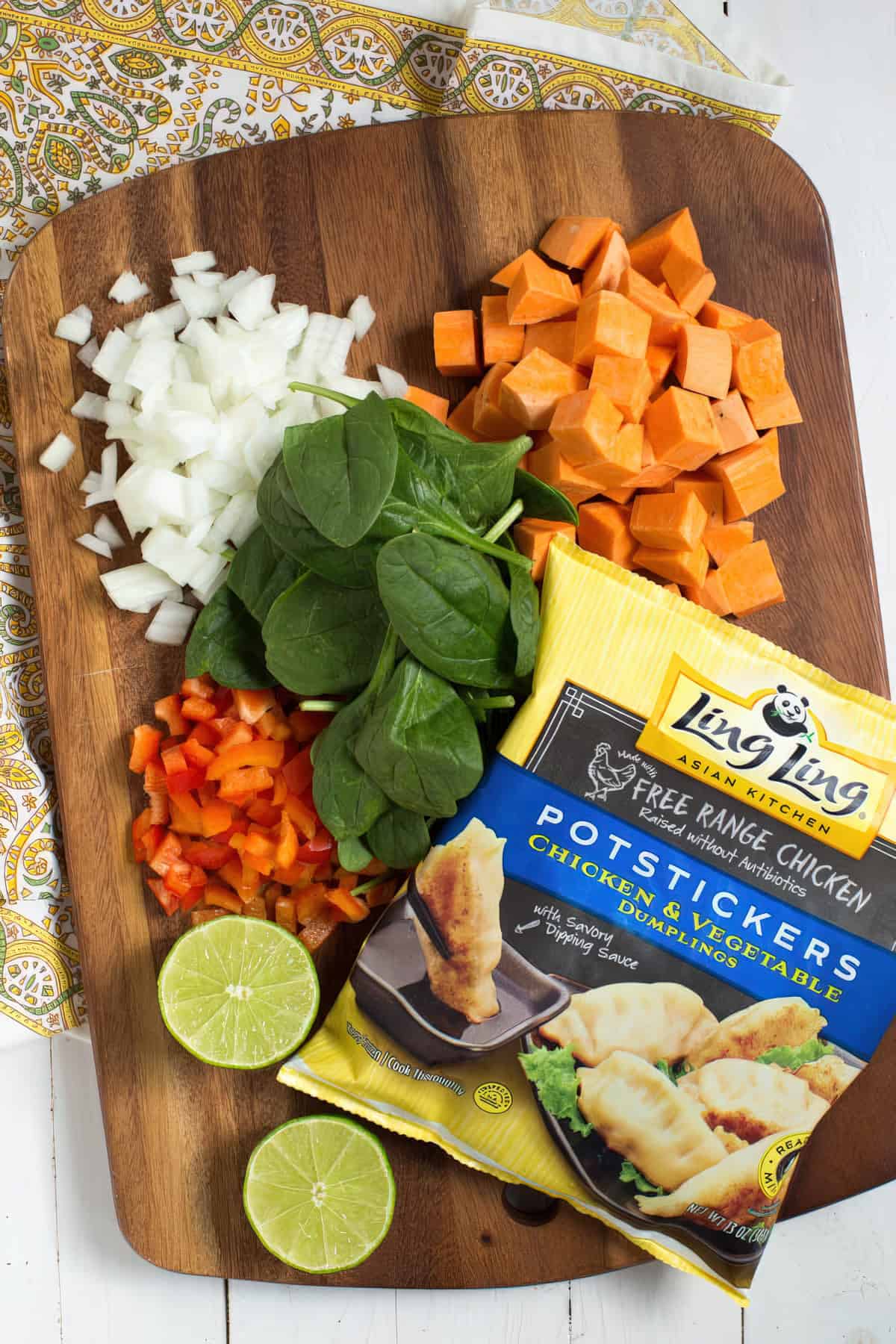 Chopped sweet potato, diced red pepper, spinach, lime halves and a bag of frozen potstickers on a cutting board