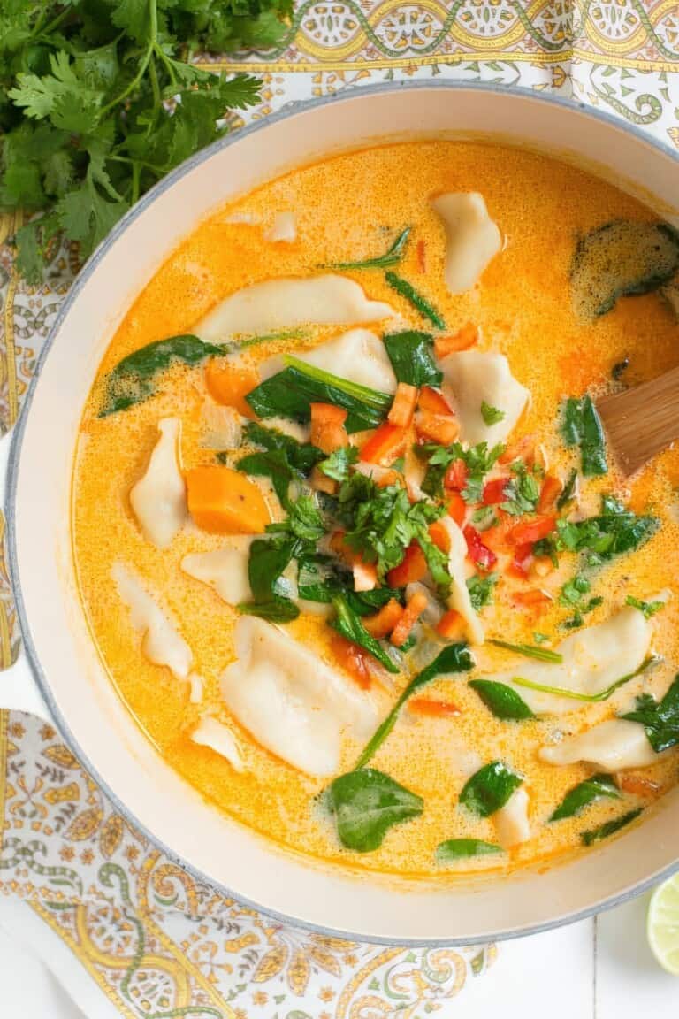 Top view of a pot with creamy coconut curry broth, potstickers and greens simmering