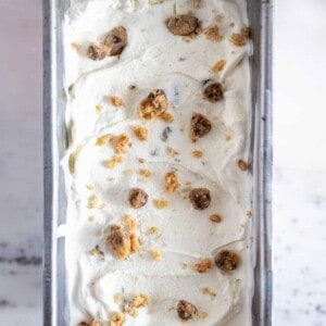 Chocolate chip cookie dough ice cream frozen in a loaf pan with cookie dough pieces on top.