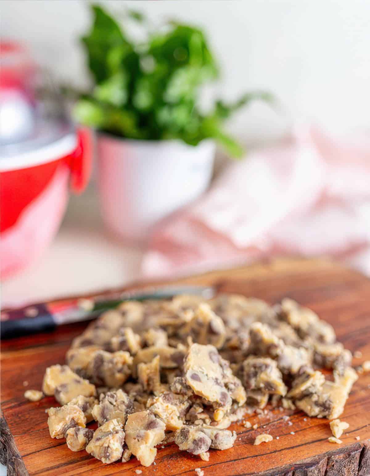 Frozen chocolate chip cookie dough chopped into bite-sized pieces on a cutting board.