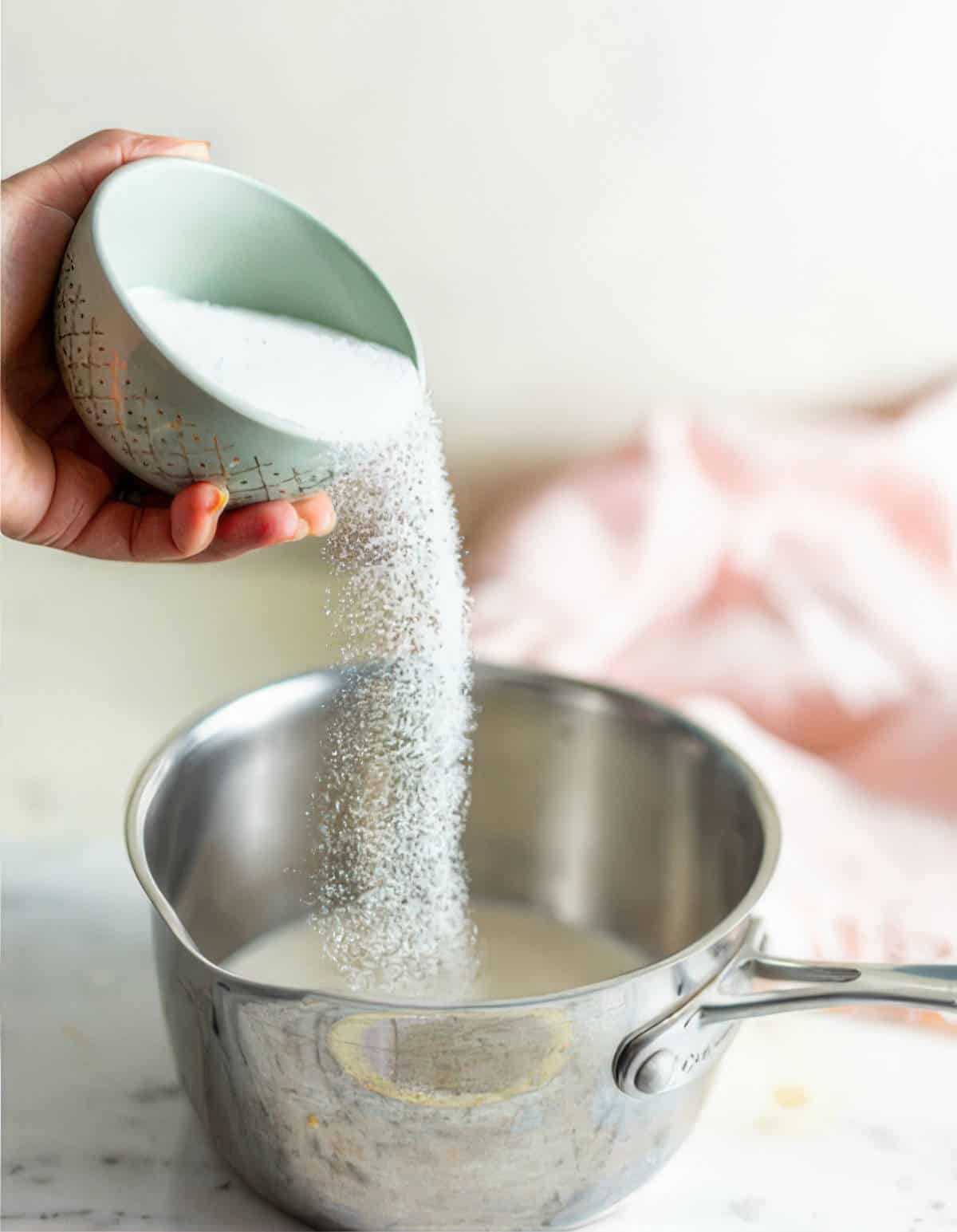 Sugar being poured into a saucepan with milk and cream to make a vanilla ice cream base.