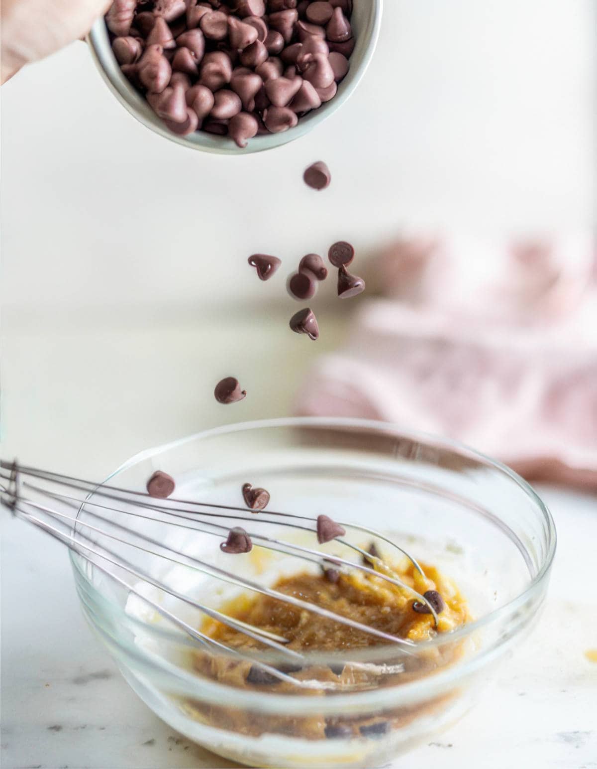 Chocolate chips being added to a bowl of cookie dough mixture while whisking.