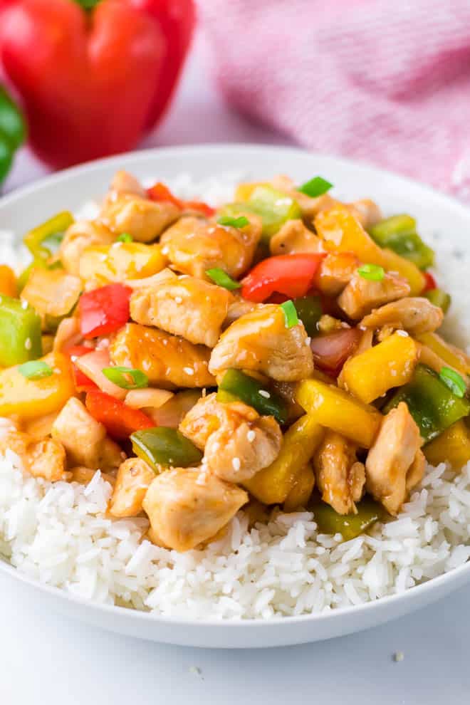 a white bowl filled with white rice and topped with sweet and sour chicken