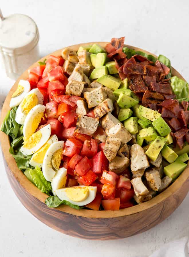a large wooden bowl with lettuce, boiled egg, tomatoes, grilled turkey, avocado and turkey bacon