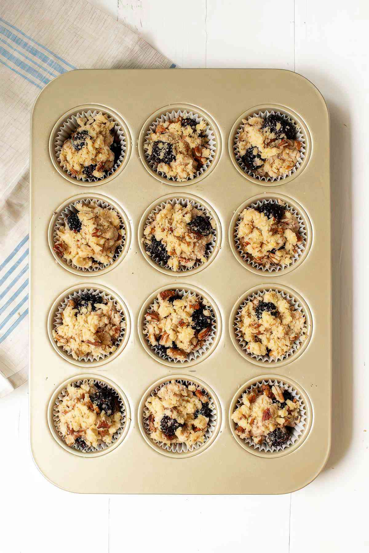 Blackberry muffin batter topped with crumble in muffin pan ready to bake