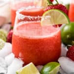 A frozen strawberry margarita in a glass with slice of lime garnish.
