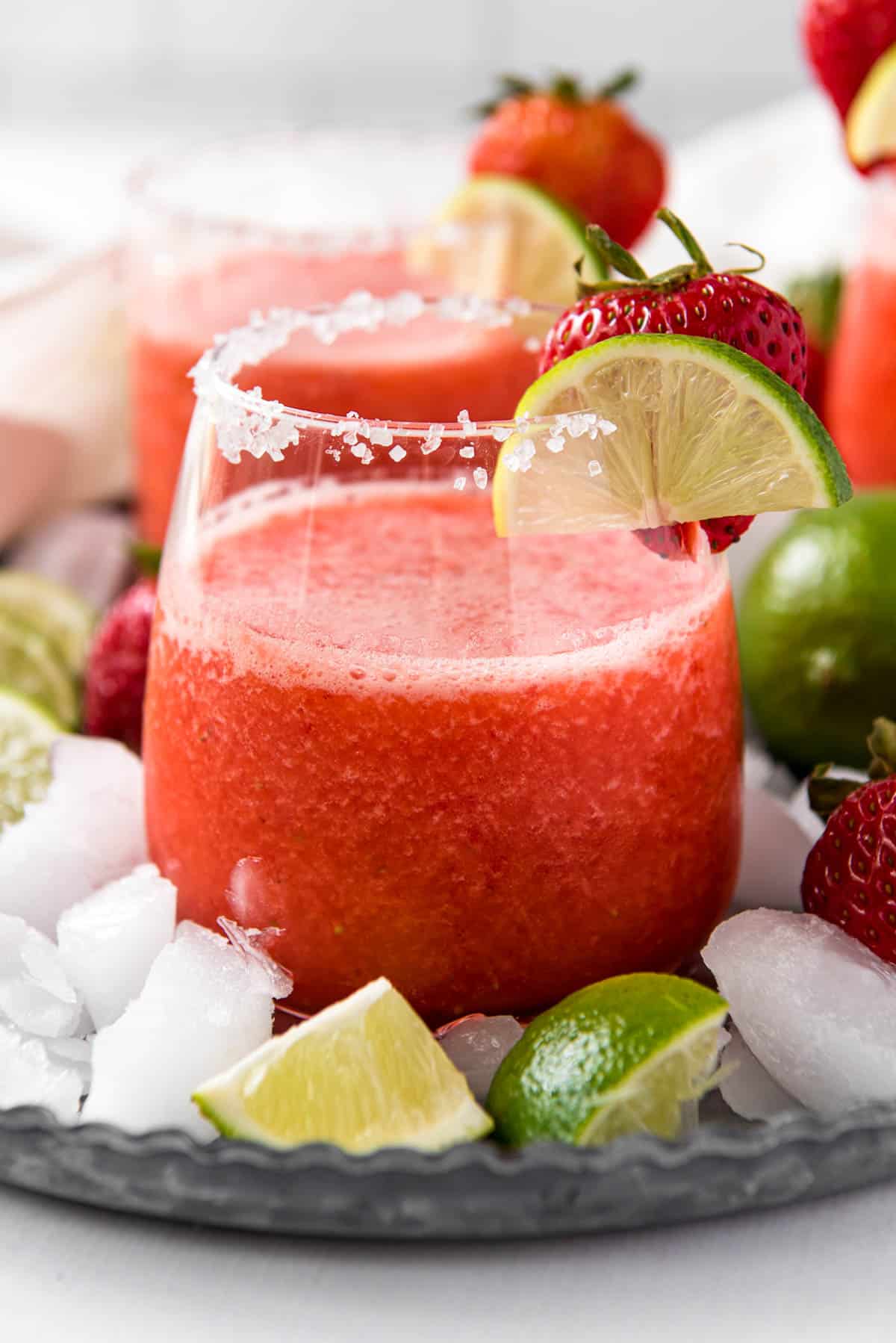 A frozen strawberry margarita in a glass with slice of lime garnish.