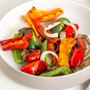 grilled peppers and onions in a white bowl on a white table