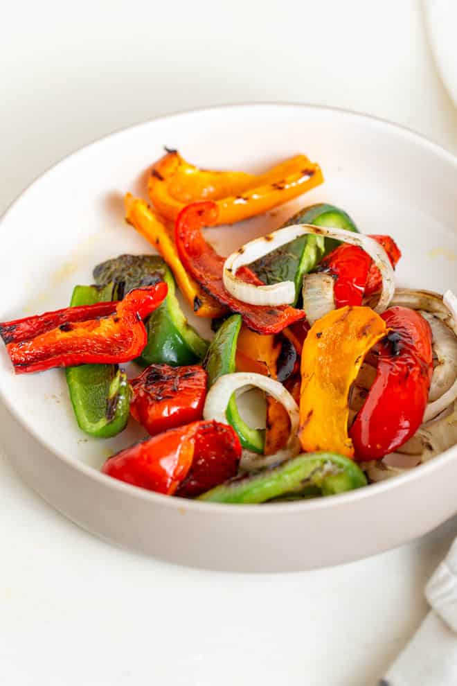 grilled peppers and onions in a white bowl on a white table