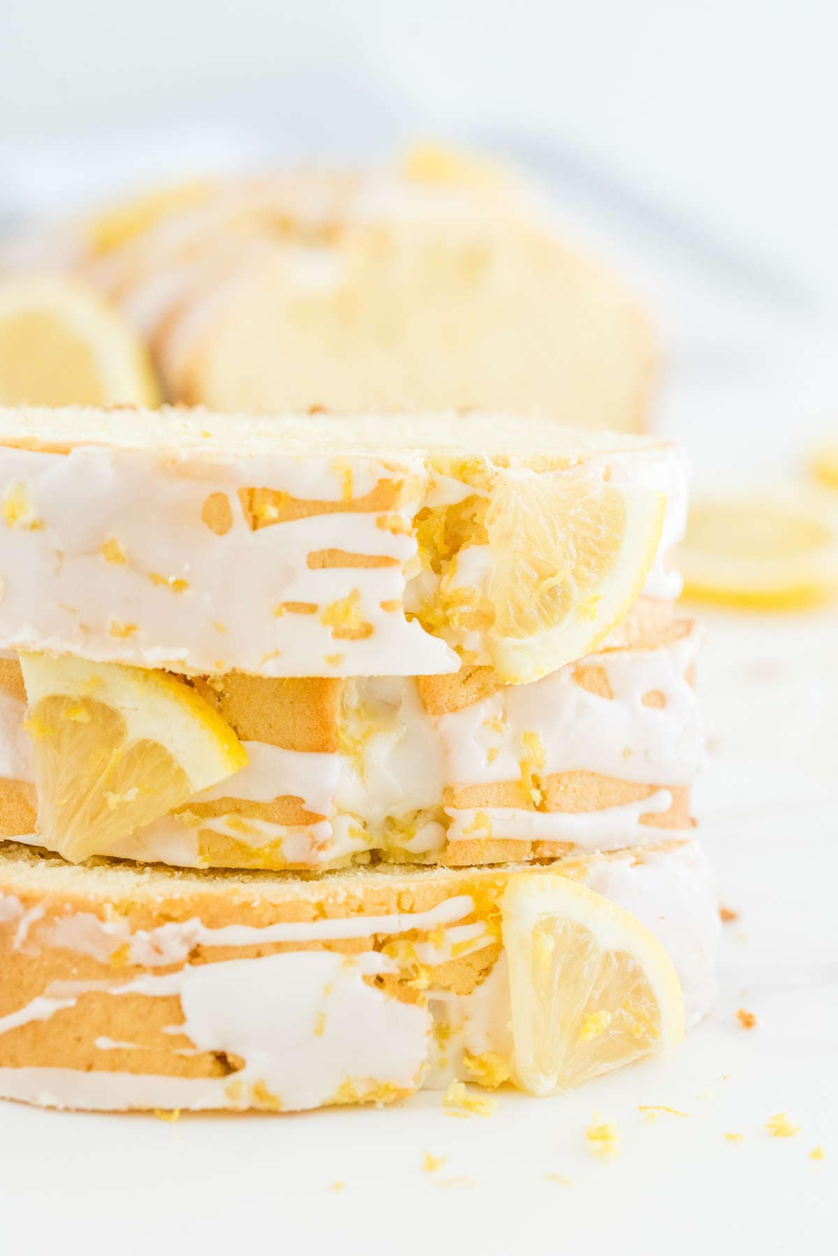 Slices of lemon loaf cake stacked with lemon glaze drizzled on top and fresh lemon wedges.