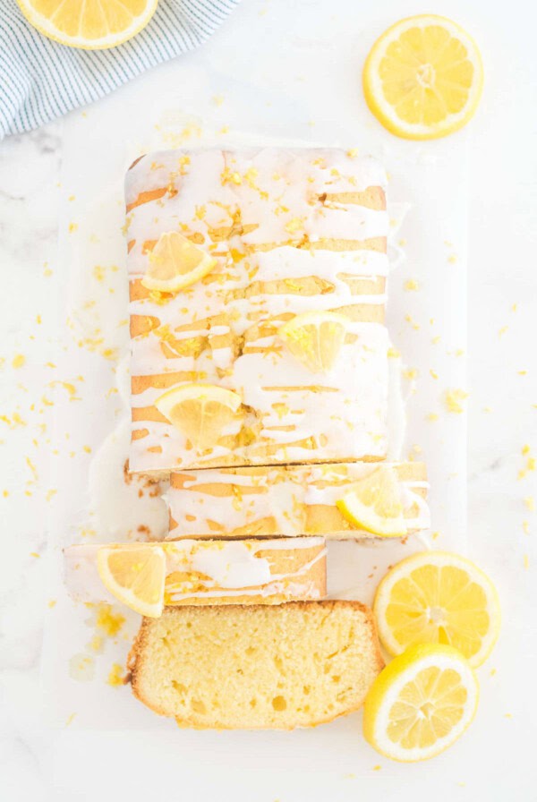 Lemon loaf cake drizzled with lemon glaze and topped with fresh lemon slices on a serving board.