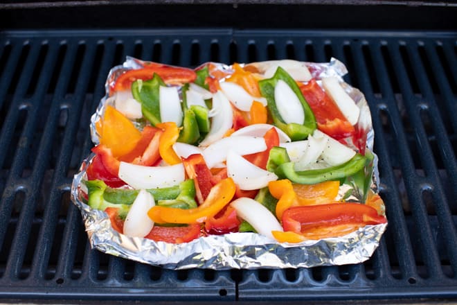 sliced bell peppers with onions in a homemade tin foil grill basket on a grill grate