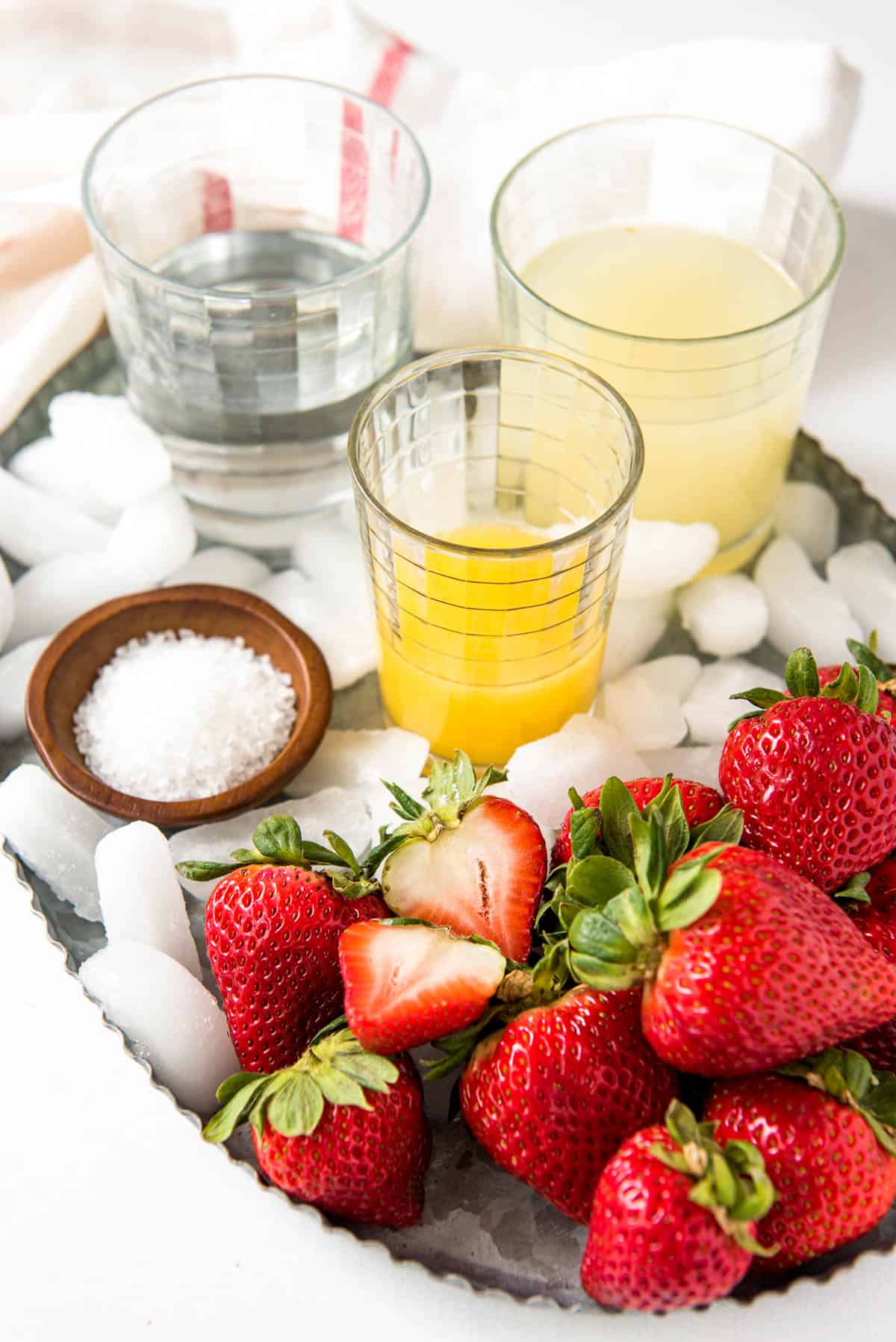 All of the ingredients for a strawberry margarita on a tray on a white counter.