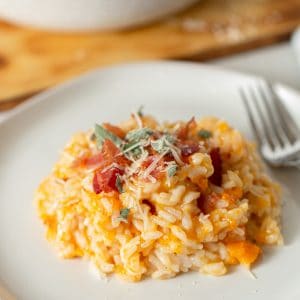 butternut squash risotto with sage and bacon on a white plate