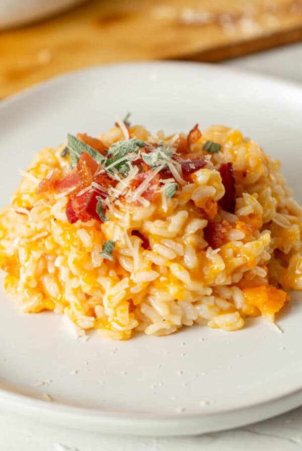 Creamy pumpkin risotto topped with crispy bacon, fresh sage, and grated Parmesan, served on a white plate.