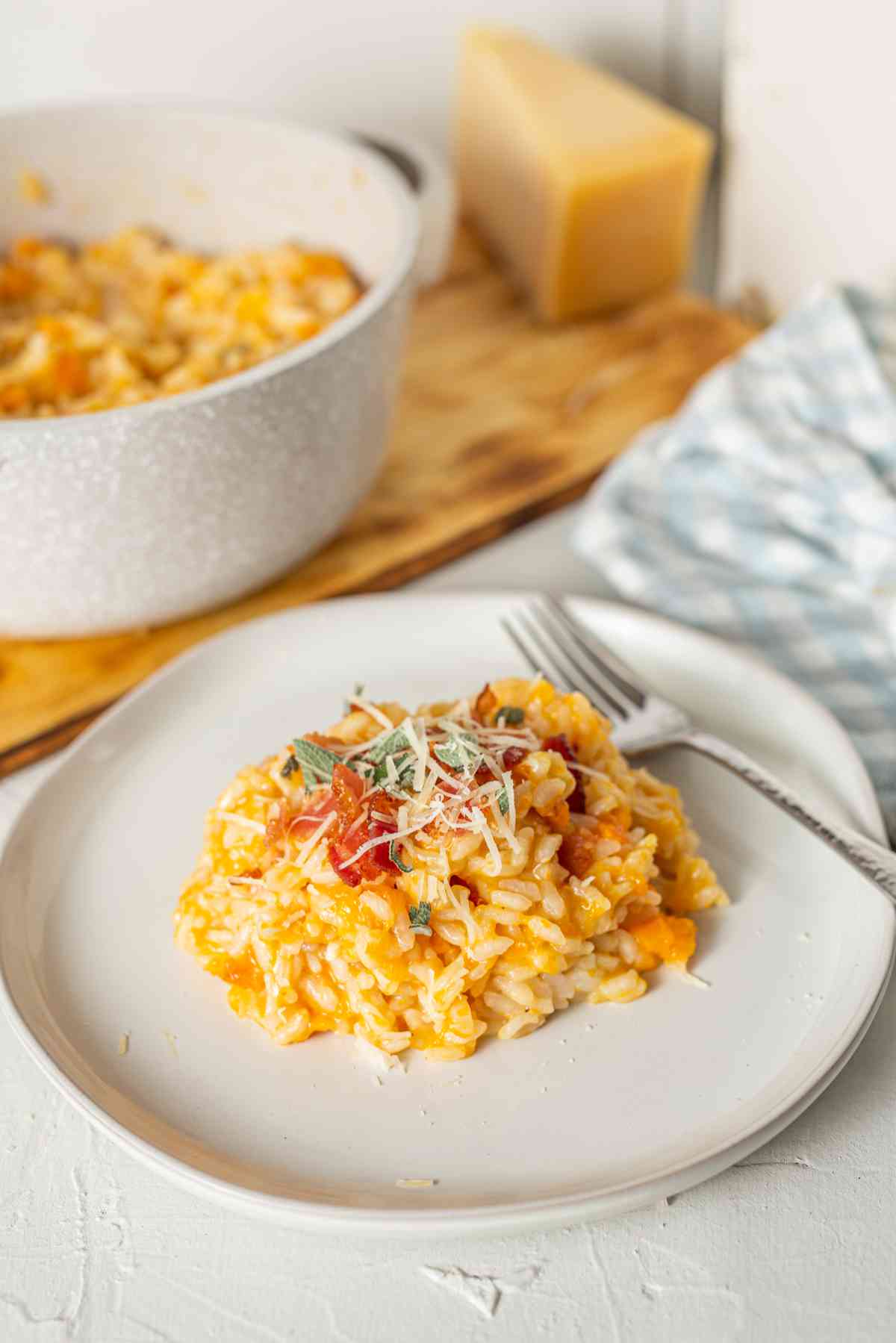 Creamy pumpkin risotto on a white plate, garnished with sage and cheese, with the pot of risotto in the background.