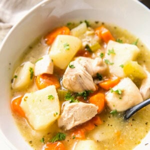 Close-up of chicken stew in a white bowl showing chunks of chicken, potatoes, carrots, and celery with parsley garnish.
