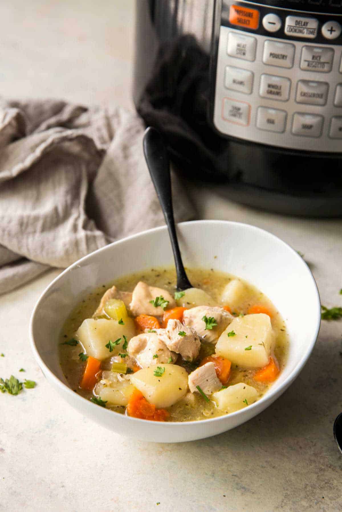 Chicken stew served in a white bowl beside an Instant Pot, filled with tender chicken and vegetables.