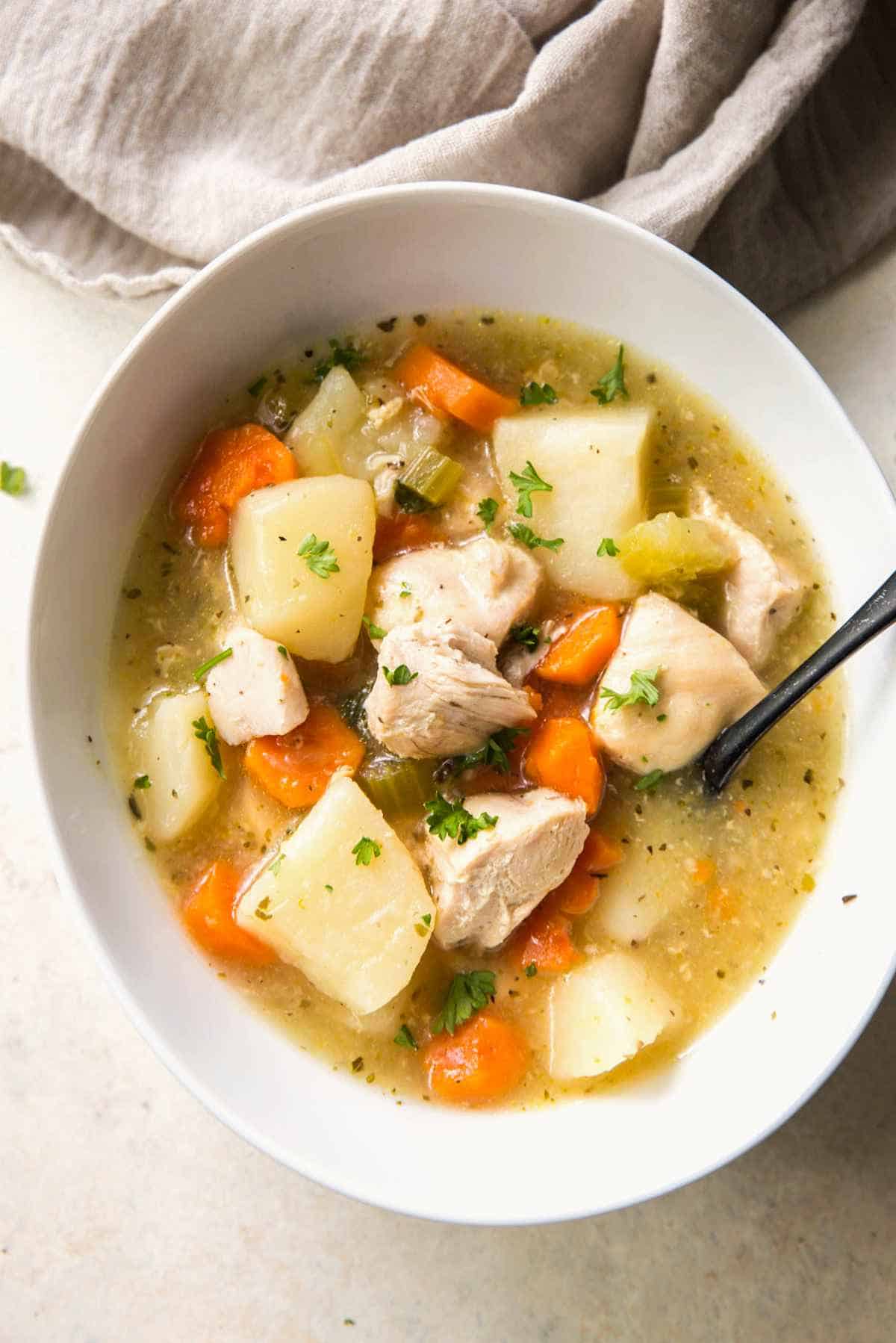 Bowl of Instant Pot chicken stew with carrots, potatoes, celery, and parsley garnish.