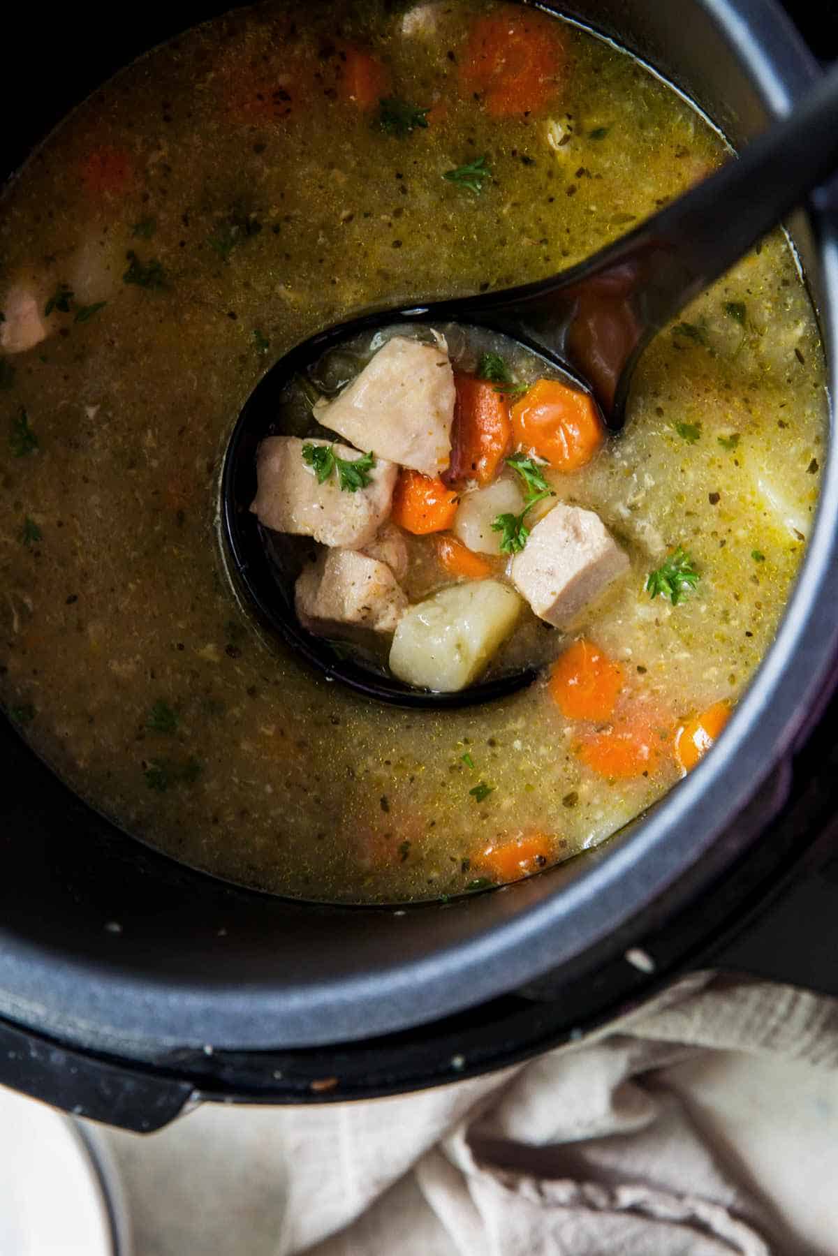 Ladle of chicken stew inside the Instant Pot with carrots, potatoes, and tender chicken in broth.