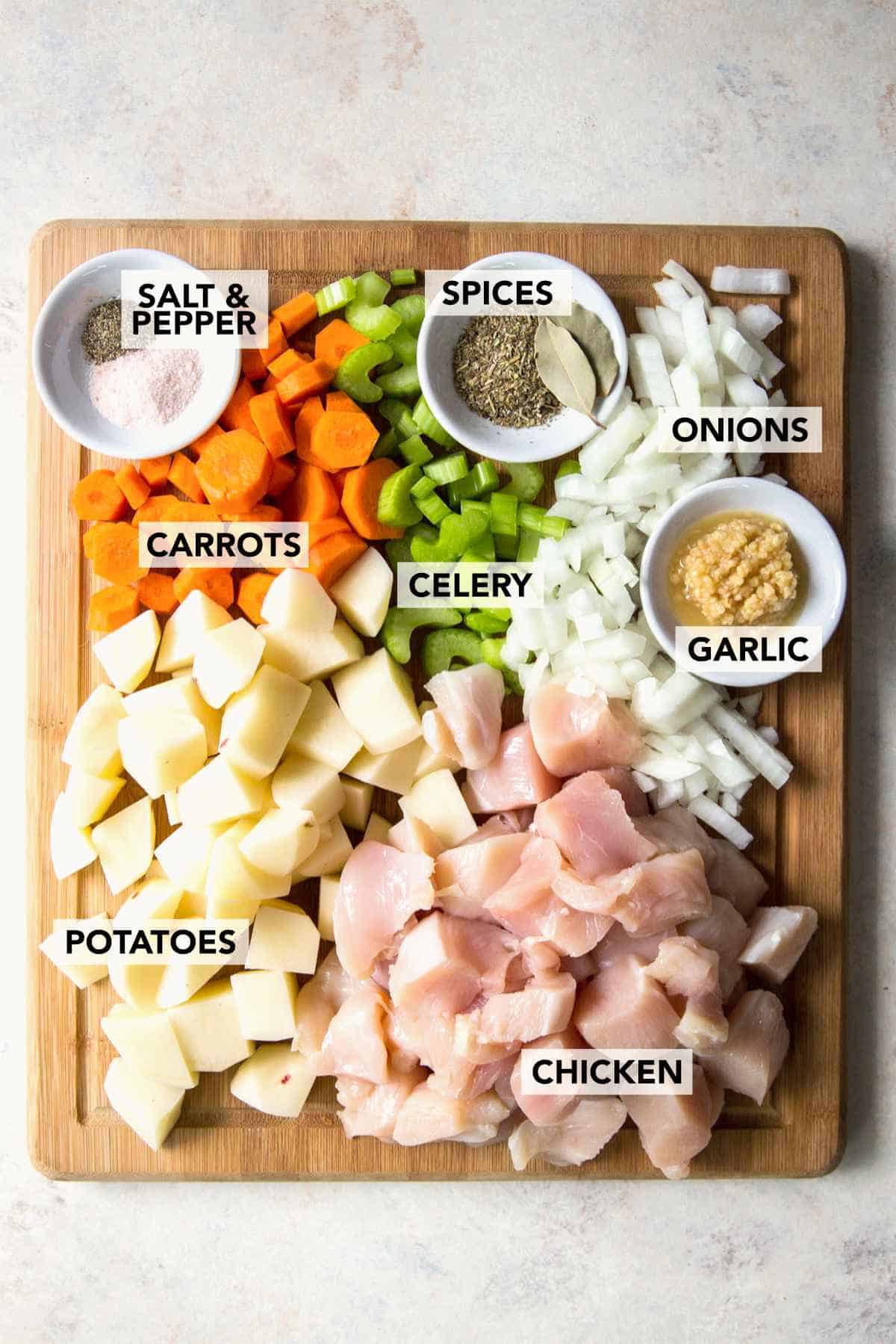 Chopped chicken, potatoes, carrots, celery, onions, garlic, spices, and seasonings arranged on a cutting board.