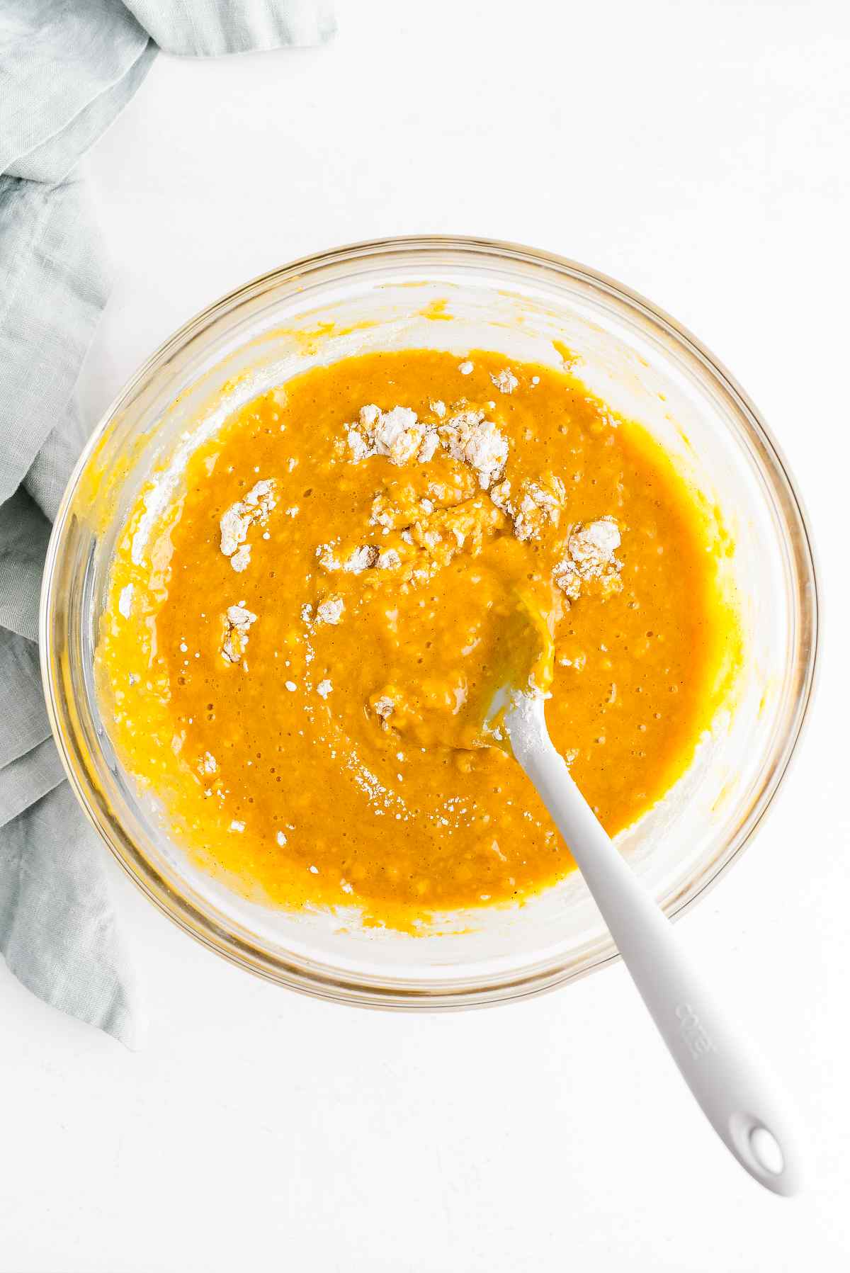 Flour being stirred into orange pumpkin donut batter in a glass bowl.