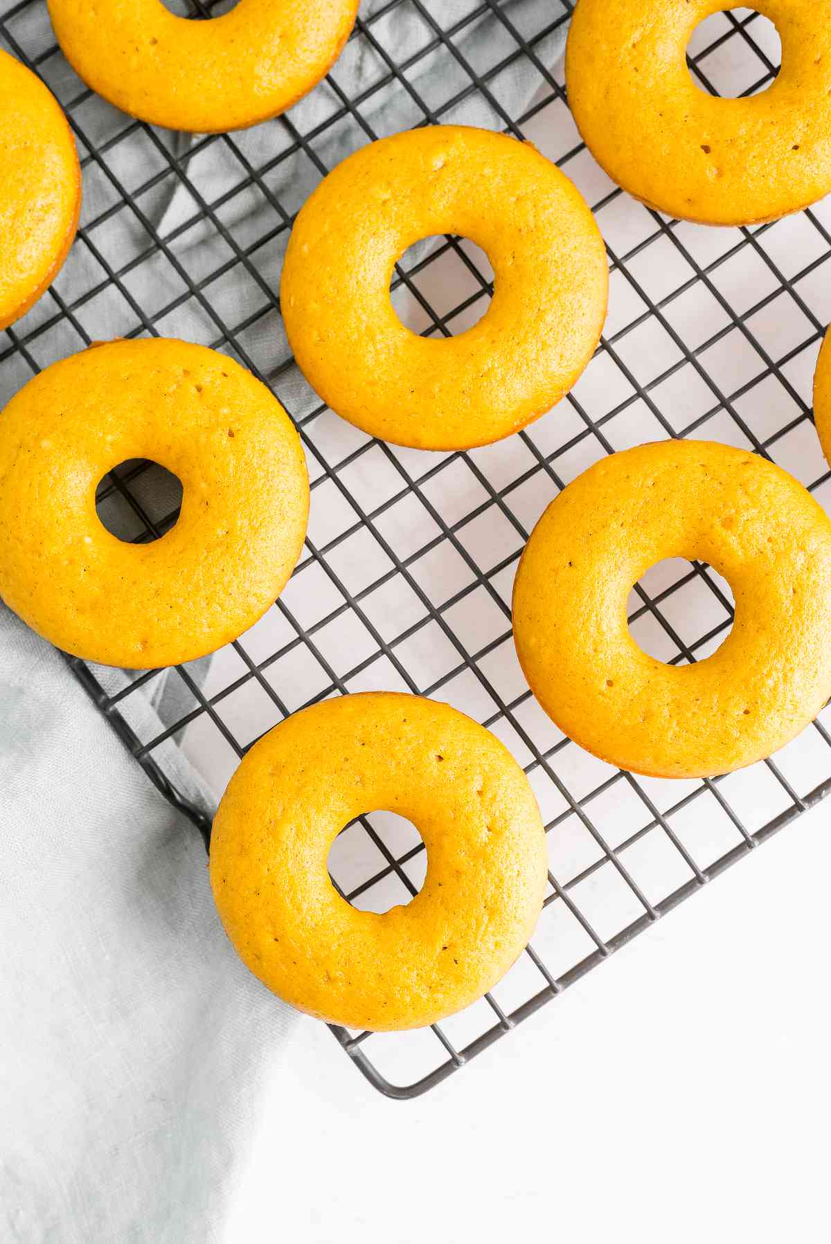 Plain baked pumpkin donuts cooling on a wire rack before adding cinnamon sugar.
