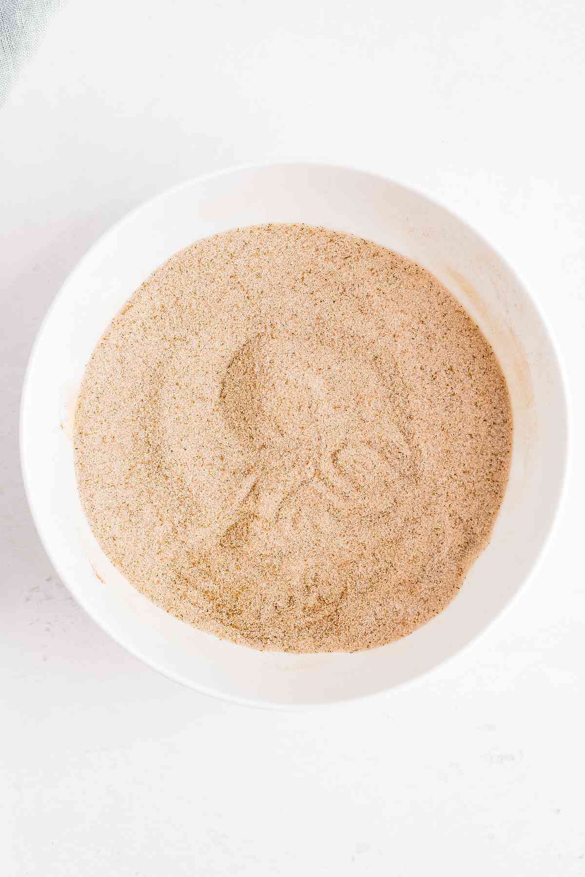 Cinnamon and granulated sugar mixed in a shallow white bowl for coating the pumpkin donuts