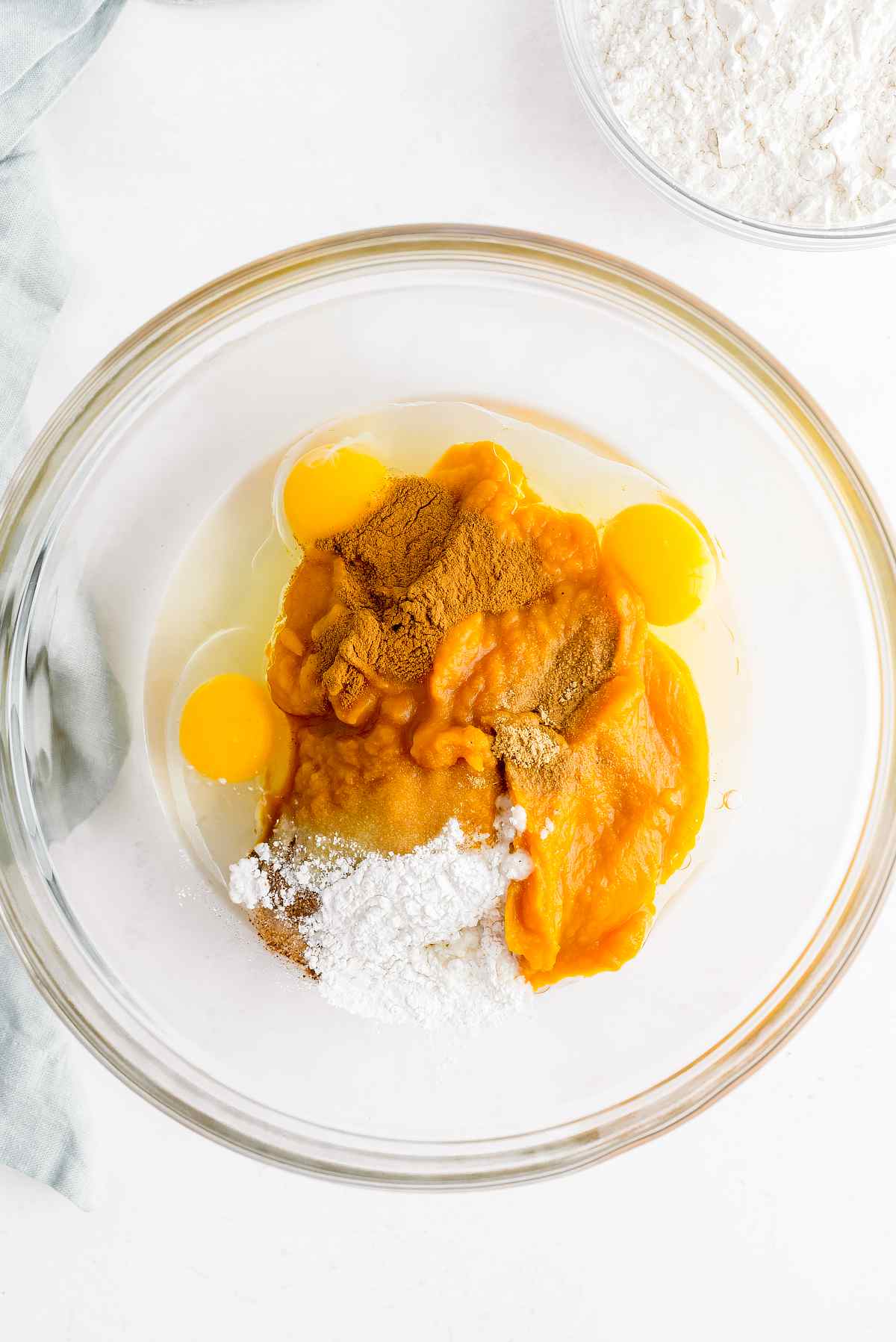 Pumpkin puree, eggs, oil, sugar, spices, vanilla and baking powder in a glass mixing bowl.