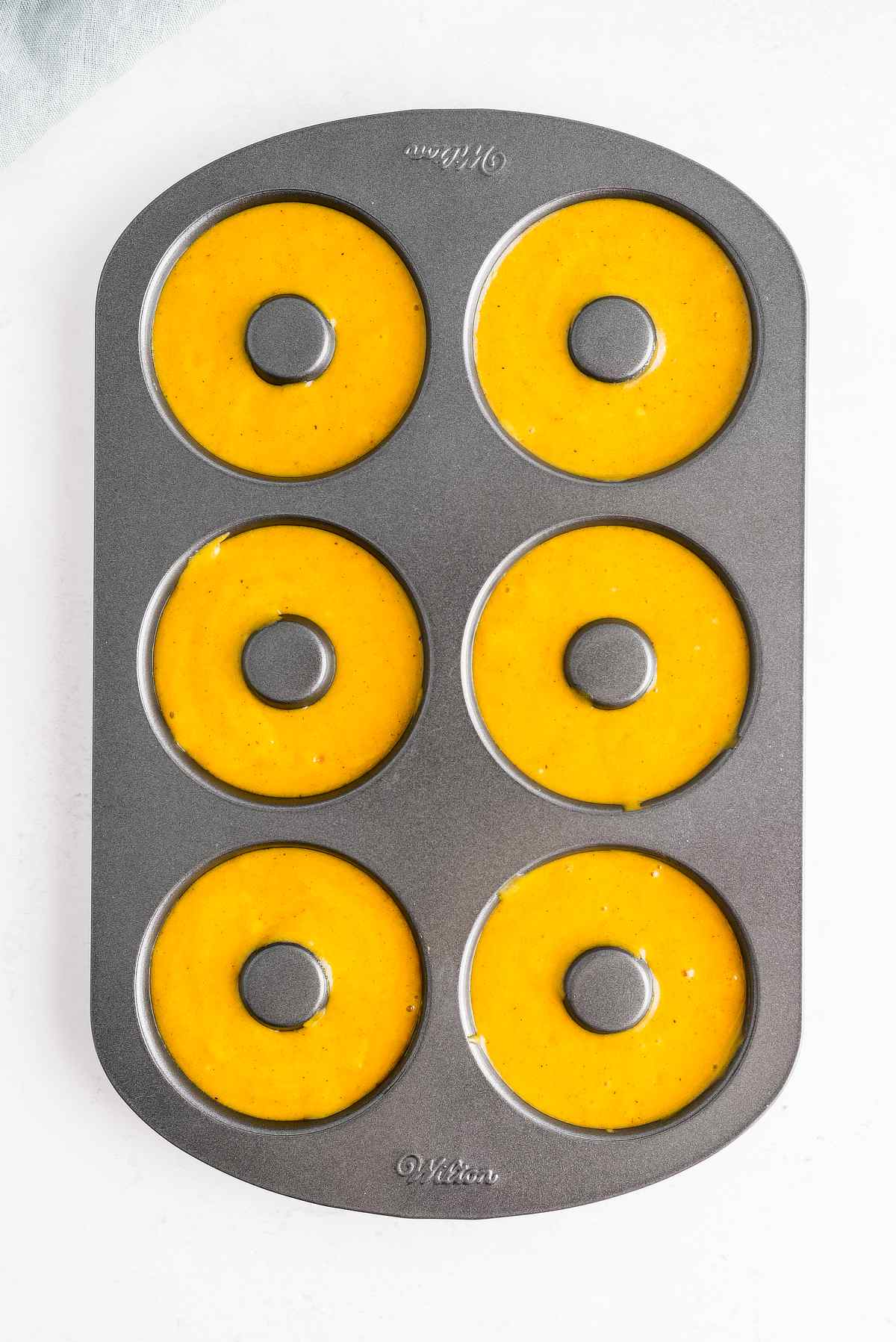 Six cavities of a donut pan filled with smooth pumpkin batter.