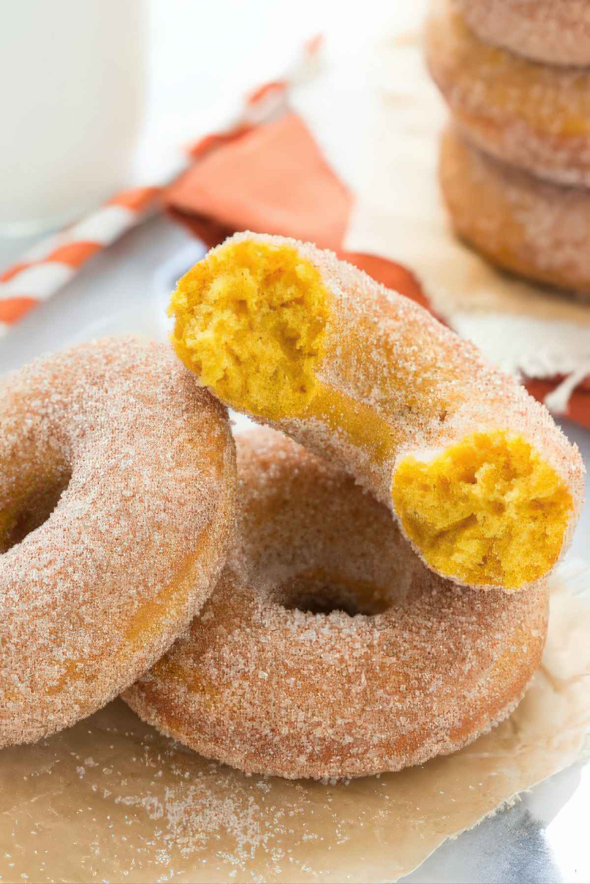 Baked pumpkin donuts coated in cinnamon sugar with one cut open to show the soft, cake-like center.