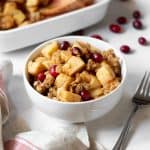 a bowl of apple, pear and cranberry crisp sitting on a table with a fork on the side