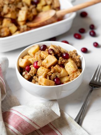 a bowl of apple, pear and cranberry crisp sitting on a table with a fork on the side