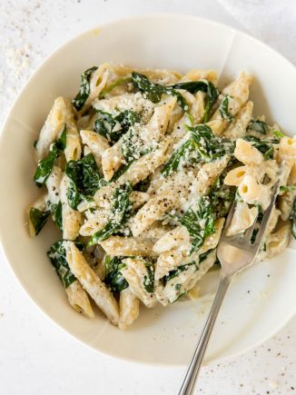 spinach and ricotta pasta in a white bowl with a fork
